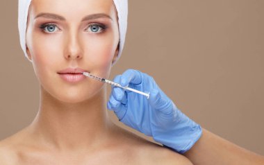Genç bir kadının güzel yüzüne iğne yapan bir doktor. Estetik ameliyat, cilt gerdirme ve estetik tıp konsepti.
