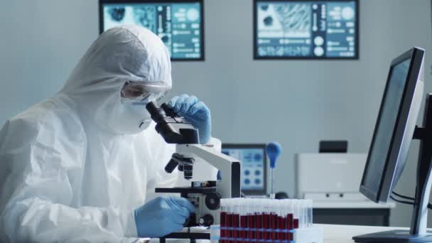 研究室の機器を使用して研究室で働く保護スーツやマスクの科学者 顕微鏡 試験管 コロナウイルス2019 Ncovハザード 医薬品の発見 細菌学とウイルス学 — ストック動画