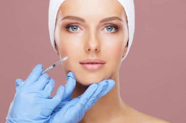 Genç bir kadının güzel yüzüne iğne yapan bir doktor. Estetik ameliyat, cilt gerdirme ve estetik tıp konsepti.