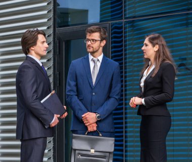 Takım çalışması ve iş konsepti. Resmi olarak kendine güvenen işadamları ofis binası önünde bankacılık ve finans piyasaları hakkında konuşuyorlar. İş adamları ve iş kadını.