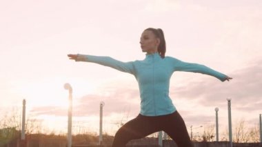 Genç, güzel ve sportif bir kadın akşam yoga eğitimi alıyor. Şehir günbatımı geçmişi. Spor ve spor konsepti.