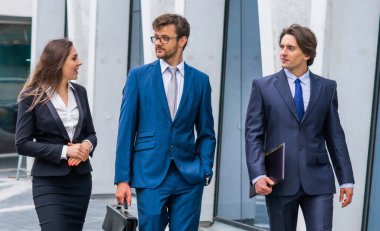 Takım çalışması ve iş konsepti. Resmi olarak kendine güvenen işadamları ofis binası önünde bankacılık ve finans piyasaları hakkında konuşuyorlar. İş adamları ve iş kadını.