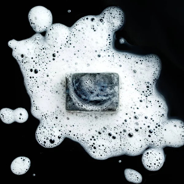 Black coal bar of soap in foam — Stock Photo, Image