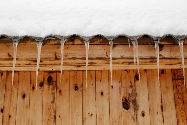 家の木造建築物の雪屋根の上のつららの行 — ストック写真
