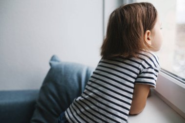 Evde oturan ve Windo 'ya bakan küçük sıkkın kız çocuğu.