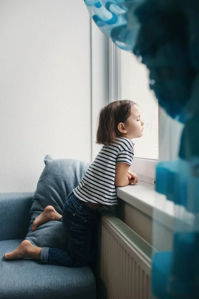 Mała znudzona dziewczyna siedzi w domu i patrzy przez okno — Zdjęcie stockowe