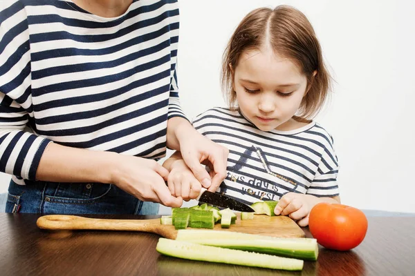Young mother teaches her little daughter to cut vegetables for h