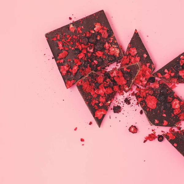 Rozgnieciony na kawałki czarny baton czekoladowy z rozproszonymi suszonymi czerwonymi jagodami — Zdjęcie stockowe