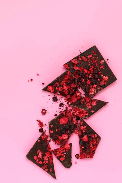 Pièces de barre de chocolat noir avec des baies rouges séchées dispersées sur pi — Photo