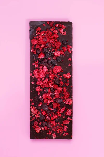 Chocolate escuro com bagas vermelhas secas em fundo rosa brilhante — Fotografia de Stock