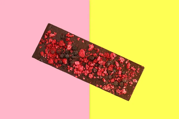 Dark chocolate bar with dried red berries on bright pink and yel — Stock Photo, Image