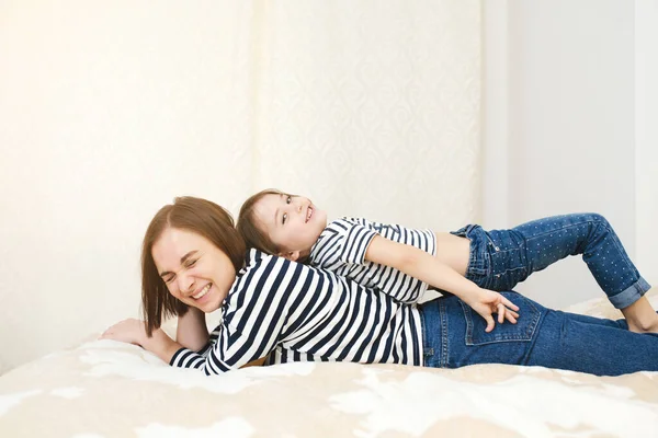 Szczęśliwa atrakcyjna matka i córeczka leżące na łóżku bawiące się razem i śmiejące, pełna długość — Zdjęcie stockowe