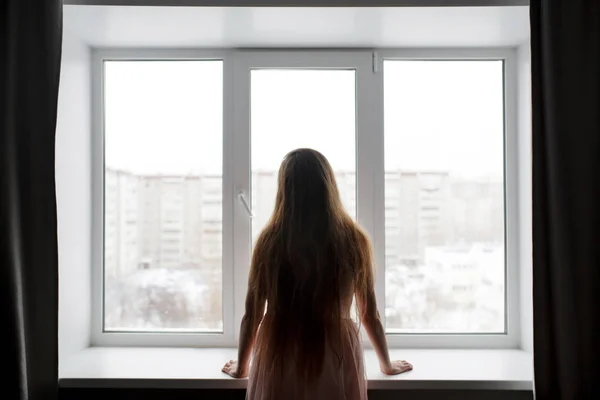 Rückansicht der Silhouette einer Frau, die am Fenster steht und nach draußen schaut, Melancholie und Krise — Stockfoto