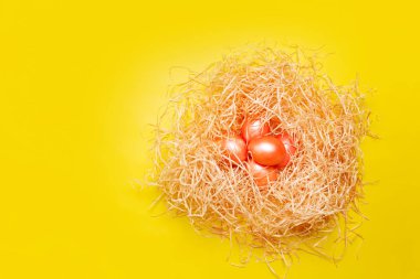 Mutlu Paskalya arkaplanı, saman yuvasında pembe ve turuncu yumurtalar parlak sarı renkte, fotokopi alanı olan üst manzara