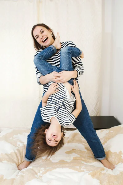 Young happy mother having fun with her cute little baby holding her upside down, playing and laughing, active games at home, full body