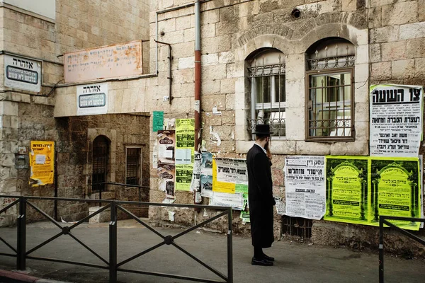 JERUSALEM, ISRAEL - 13 Ekim 2013: Kudüs, İsrail 'de Mea Shearim caddesinde dikilen geleneksel takım elbiseli tanınmayan ortodoks Yahudi adam, duvarlardaki yazıları okuyor.
