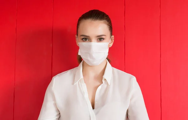 COVID-19 Coronavirus pandemico Donna con maschera protettiva per la diffusione del virus della malattia SARS-CoV-2. Ragazza con maschera chirurgica sul viso contro la malattia di Coronavirus 2019, su sfondo rosso Immagine Stock