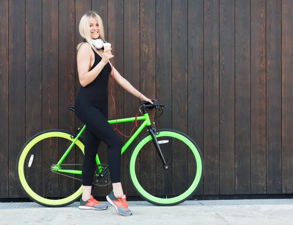 Sexy chica rubia en negro ataduras vestidos comiendo helado en un día de verano junto a una brillante bicicleta fija —  Fotos de Stock