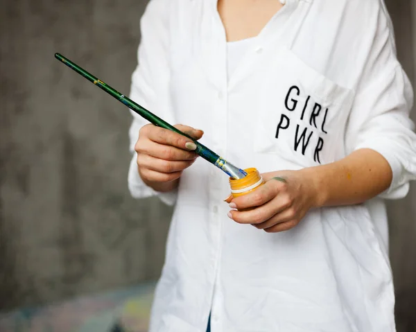 Vrouwelijke kracht van kunst. De kunstenares houdt een penseel en verf vast. Wit shirt. De kunstenaar haalt inspiratie uit. Rechtenvrije Stockafbeeldingen