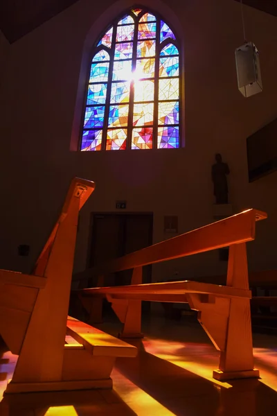 Vidros manchados modernos refletindo cores em bancos de igreja — Fotografia de Stock