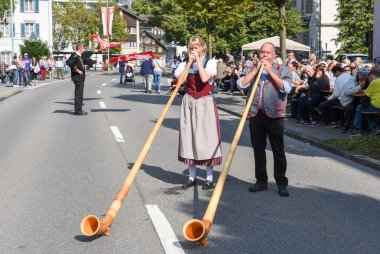 Geleneksel giyim eşyası ve alphorn oynayan insanlar  