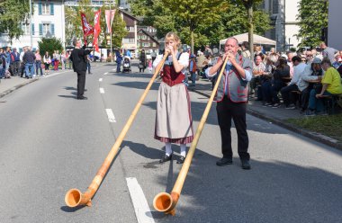 Geleneksel giyim eşyası ve alphorn oynayan insanlar  