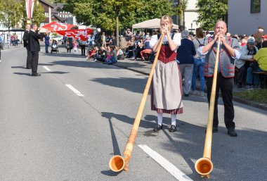 Geleneksel giyim eşyası ve alphorn oynayan insanlar  