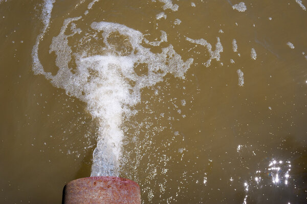 Water flowing from rusted pipe into brown water.