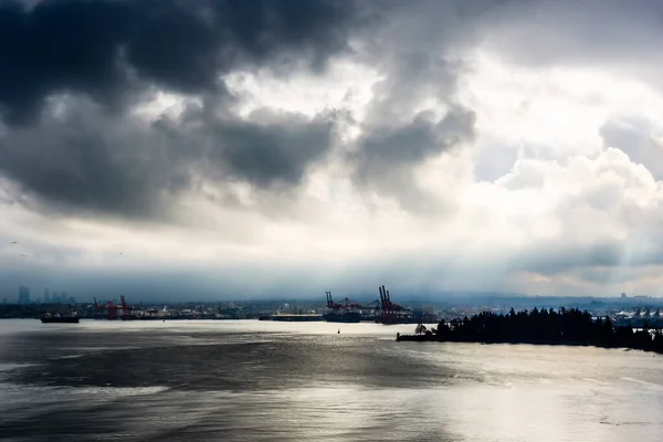 Vancouver, British Columbia, Kanada 'daki su üzerinde yüksek kontrastlı kara bulutların ardından güneş doğuyor..