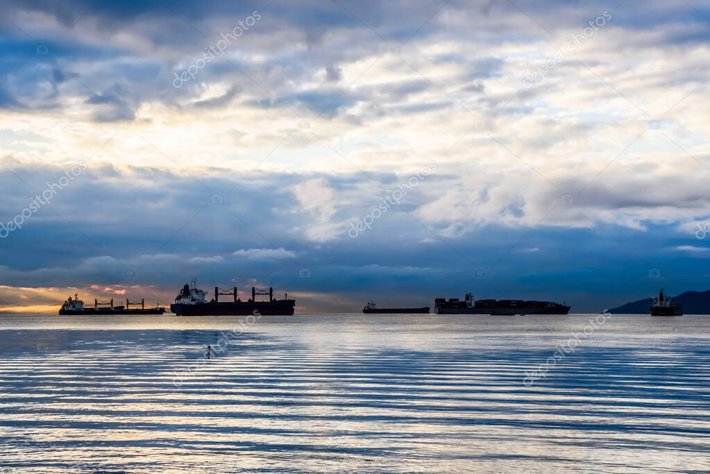 Cargo ships anchored in bay under cloudy sky at dusk near Vancouver, British Columbia, Canada.