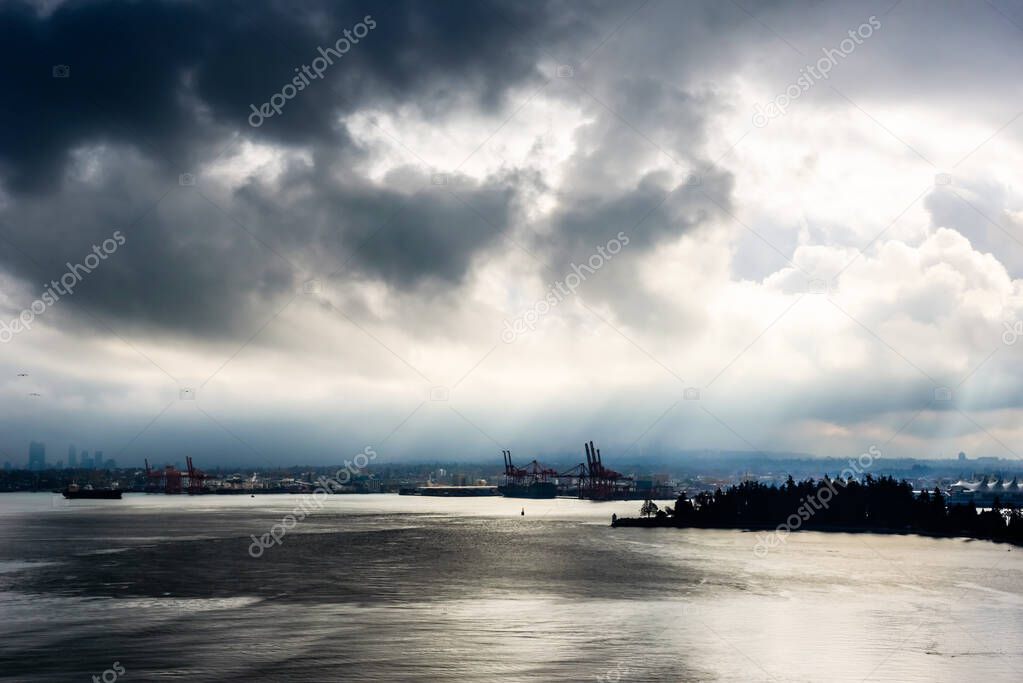 Sun breaking through from behind dark clouds in high contrast over water in Vancouver, British Columbia, Canada.