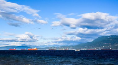 Kargo gemileri ve diğer tekneler Vancouver, British Columbia, Kanada yakınlarında birkaç bulut ve mavi gökyüzünün altında demirlediler..