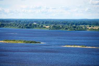 Nehir manzarası. Mavi derin su ve hızlı akım. Diğer kıyıda yeşil çalılıklar.
