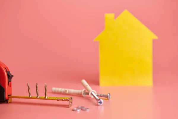 Home repair and redecorated concept. House renovation. Screws and yellow house shaped figure on pink background. — Stock Fotó