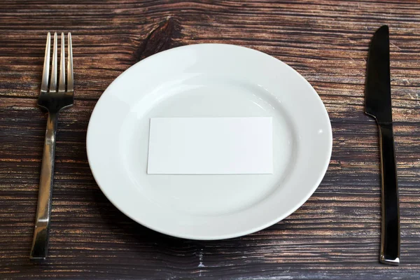 Lege bord op tafel met bestek en blanco visitekaartje, bovenaanzicht. Bericht voor bezoeker van restaurant of café. Zakelijke lunch zonder tips concept. — Stockfoto