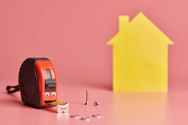 House renovation funny concept. Metal tape measure and other repair items. Home repair and redecorated concept. Yellow house shaped figure on pink background. — Stok fotoğraf