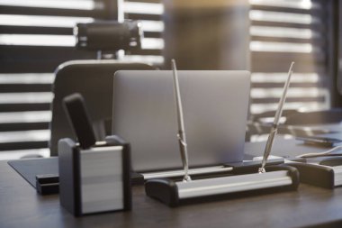 Modern ofis işyeri. İş yerinde şef, patron ya da diğer çalışanlar için iş bilgisayarı var. Defter çalışma masasında. Ofis büyük bir şirket. Işıklar yarı açık panjurlarda.