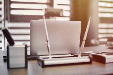 Modern ofis işyeri. İş yerinde şef, patron ya da diğer çalışanlar için iş bilgisayarı var. Defter çalışma masasında. Ofis büyük bir şirket. Işıklar yarı açık panjurlarda.