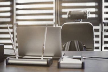 Modern ofis işyeri. İş yerinde şef, patron ya da diğer çalışanlar için iş bilgisayarı var. Defter çalışma masasında. Ofis büyük bir şirket. Işıklar yarı açık panjurlarda.