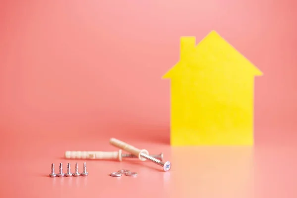 House renovation concept. Home repair and redecorated. Screws and yellow house shaped figure on pink background.