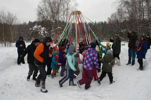 Karnaval kutlama. İnsanlar, çocuklar, kurdeleler kış hava yağlı atlıkarınca çevresinde elinde tutan bir daire içinde çalıştırmak animatörler. Rusya Federasyonu şehir Moskova, Zelenograd, 18 Şubat 2018.