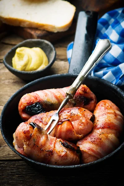 Sausages with prunes and bacon in iron pan — Stock Photo, Image