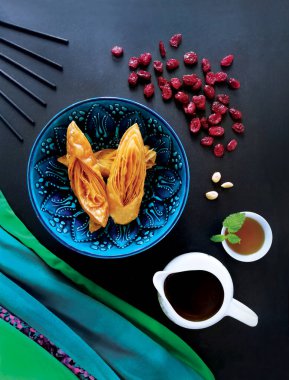 Doğu tatlıları, mavi bir kasede baklava, kurutulmuş kızılcık ve çay. Siyah bir arka planda hayat, üst görünüm
