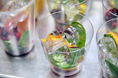 Plastik bardakta mojito. 2 şişe mojito şurubu. Mojito içerikli boş bardaklar. Bardakta buz küpleri. Sıvı nitrojenden gaz.