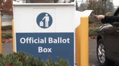 Person pulls up to official ballot box and inserts envelopes to vote on election day.