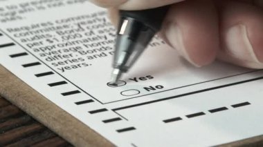 Close up of person voting yes on official ballot.