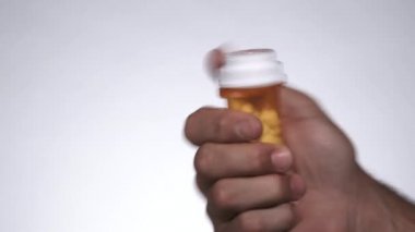 Close up of person unscrewing medication container and dumping out all the pills then leaving frame in studio.