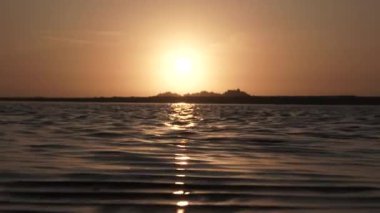 Sun refelecting on flowing water at sunset with ocean waves crashing on shore.