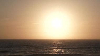 Camera panning shot on sun shining above ocean horizon to static shot of sun centered to wide angle zoom out beach scenic.