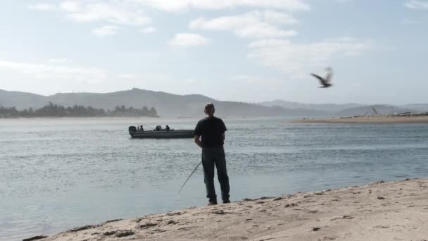 Older Man Standing Shore Casting Bay Fishing Boat Passing — Stockvideo